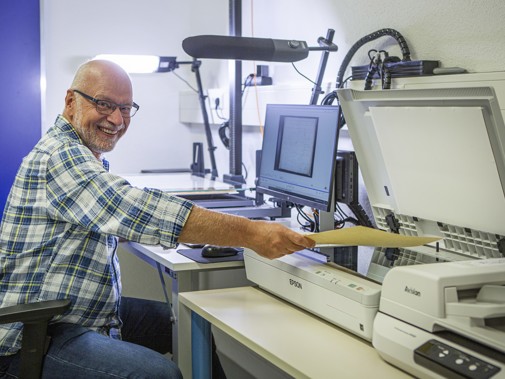 Digitalisering: man achter laptop en naast scanner scant een formulier.