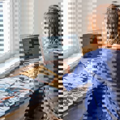 vrouw werkt op laptop achter bureau met boek en floppydisks naast zich