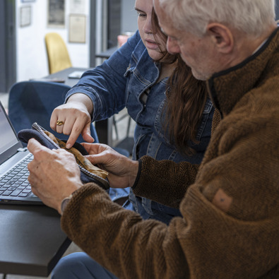 Twee personen kijken naar een object. Op de achtergrond staat een laptop, om dit object in te voeren en te omschrijven.