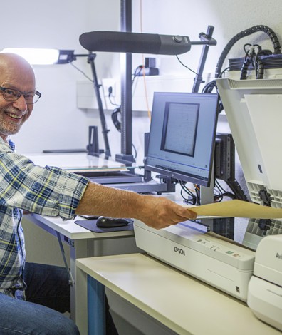 Digitalisering: man achter laptop en naast scanner scant een formulier.