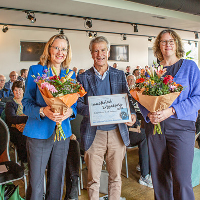 De uitreiking van Immaterieel Erfgoedprijs door voorzitter Erik Kopp (midden) aan Ellen Steendam (links) en Marloes Wellenberg (rechts) met een oorkonde en bloemen.