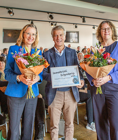 De uitreiking van Immaterieel Erfgoedprijs door voorzitter Erik Kopp (midden) aan Ellen Steendam (links) en Marloes Wellenberg (rechts) met een oorkonde en bloemen.