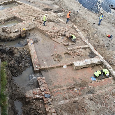 Archeologische put met restanten van muren van een kloostergebouw en archeologen aan het werk