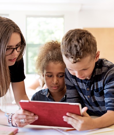 Kinderen kijken met leraar in de klas op tablet