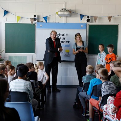 Man en vrouw staan voor klas waar leerlingen zitten