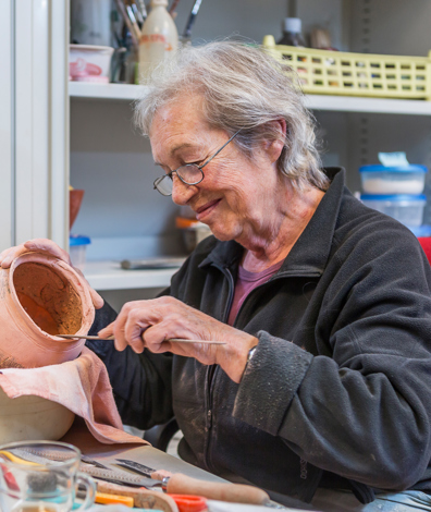 Vrouw zit aan tafel met gereedschap en aardewerken kruik