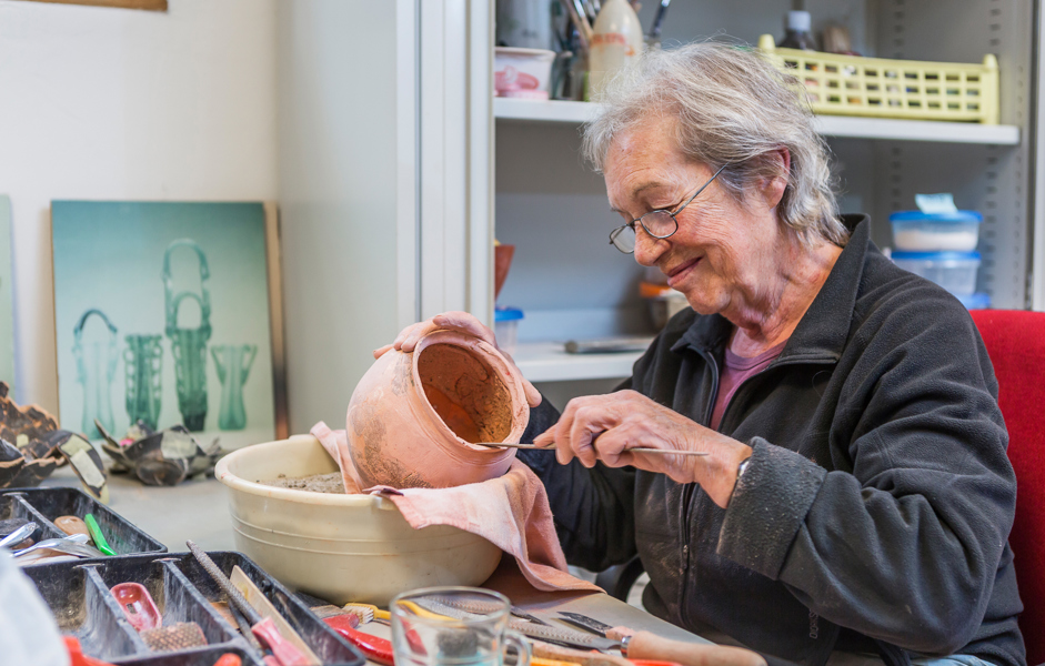 Vrouw zit aan tafel met gereedschap en aardewerken kruik