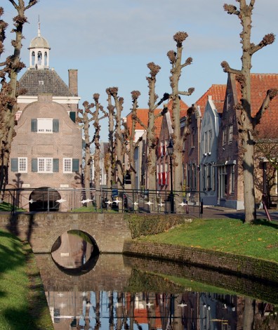 Gracht met gras en bomen en op achtergrond een monument