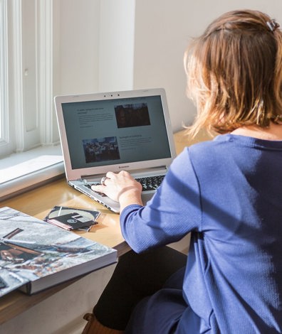 vrouw werkt op laptop achter bureau met boek en floppydisks naast zich