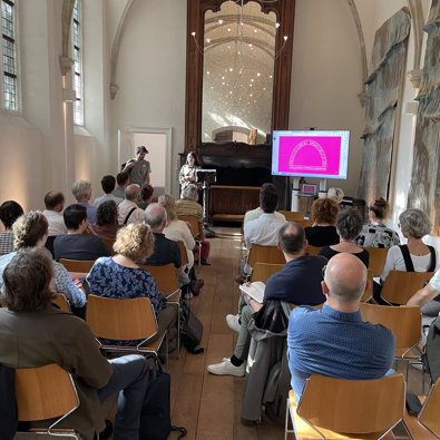 Foto achterin de Van Assendelftkapel gericht op het podium en publiek, de zaal waar de bijeenkomst gehouden werd.