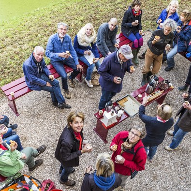 Grote groep mensen zit in tuin en drinkt koffie