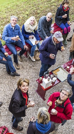 Grote groep mensen zit in tuin en drinkt koffie