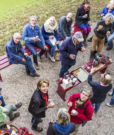 Grote groep mensen zit in tuin en drinkt koffie