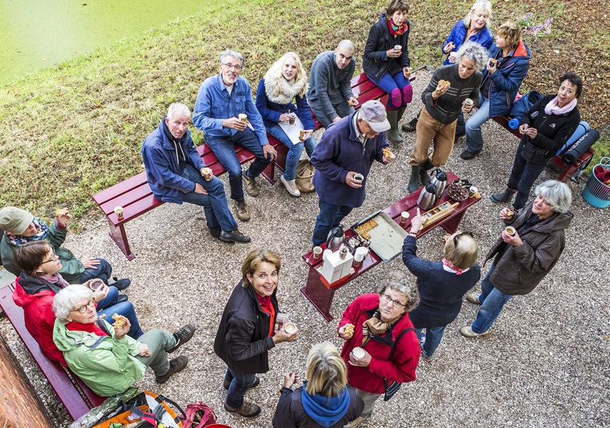 Grote groep mensen zit in tuin en drinkt koffie