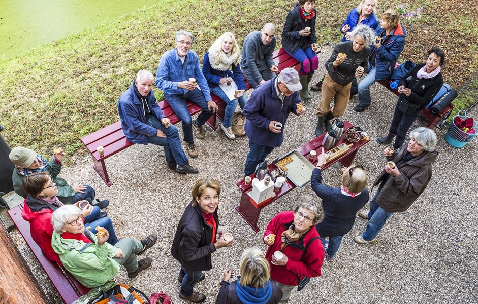 Grote groep mensen zit in tuin en drinkt koffie