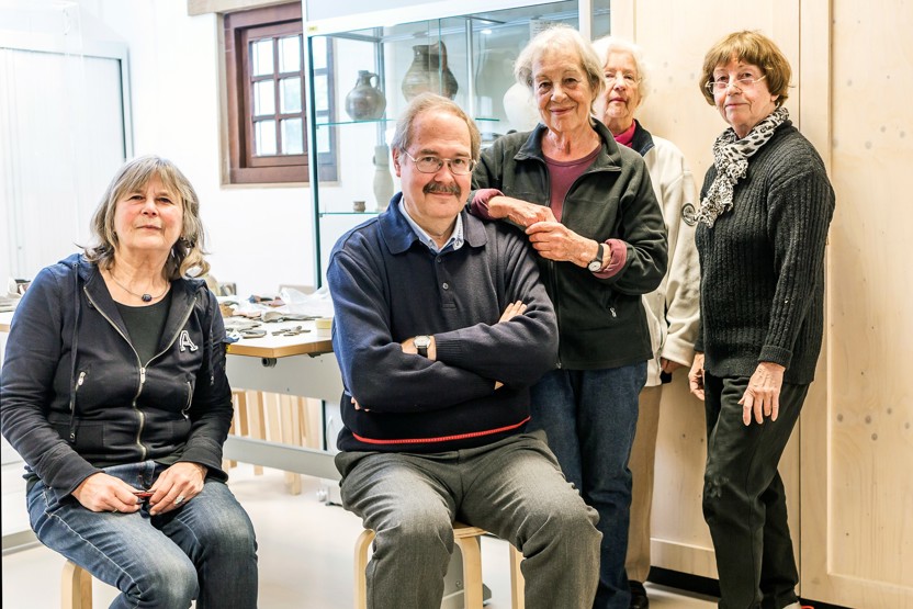 Twee mensen zitten op krukken en drie mensen staan in ruimte