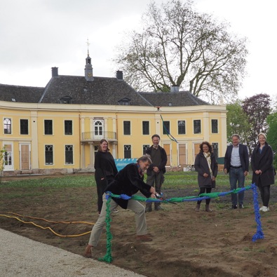 groep mensen staat voor een gele villa, man knipt een groenblauw lintje