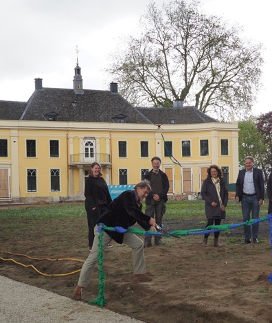 groep mensen staat voor een gele villa, man knipt een groenblauw lintje