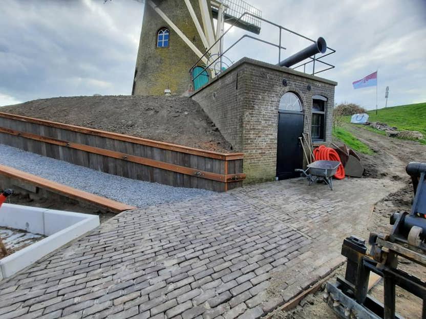 Onderaan de molen staat het gerestaureerde motorhuis met de scharnierende pijp voor de stoomaandrijving en links de nieuw aangebrachte helling voor mindervaliden.