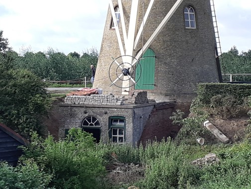 Restauratie in uitvoering, het metselwerk van het motorhuis is op deze foto net hersteld. Er wordt een isolerende vochtwering aangebracht tussen de muur van het motorhuis en het talud van het molenerf.